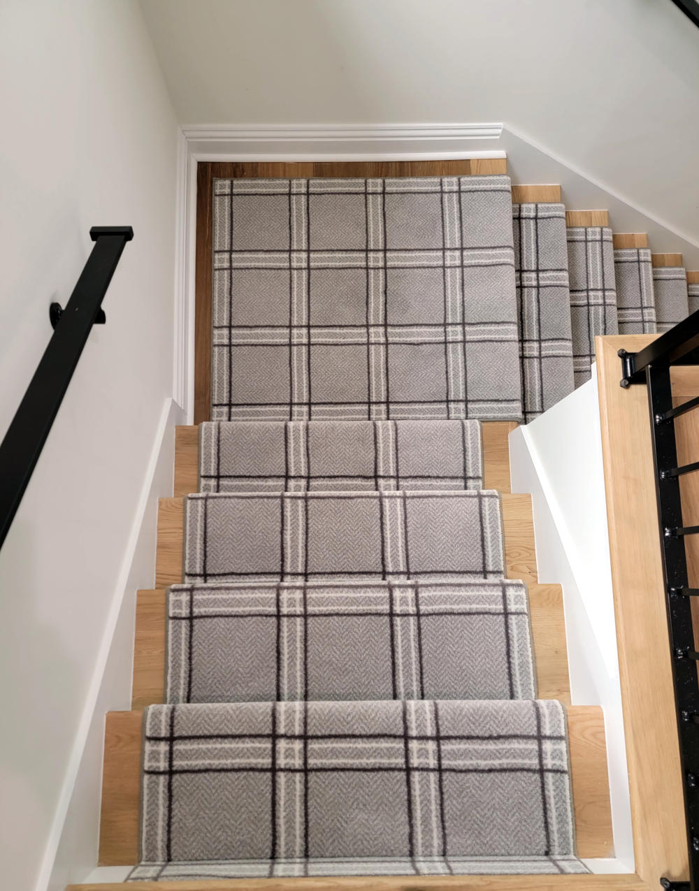 A gray rug with herring bone stitching and a square pattern on a carpet descending wooden stairs. 